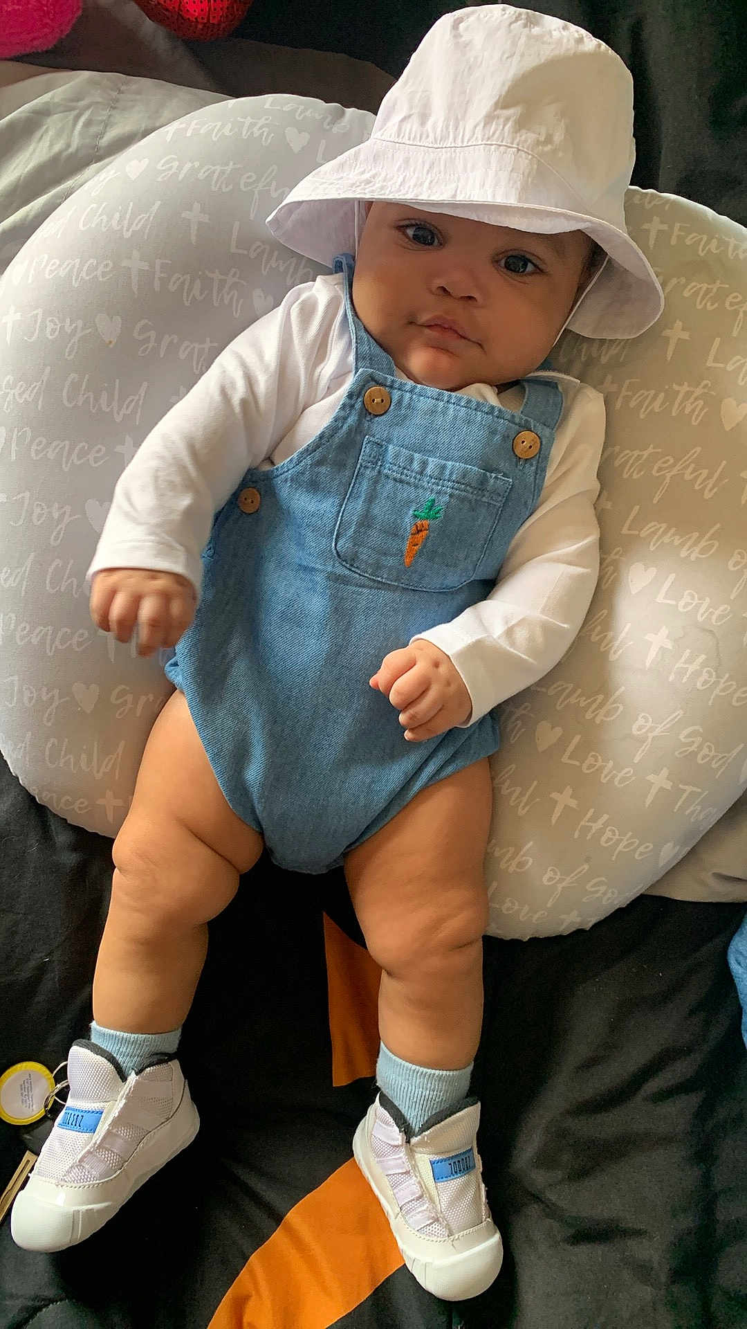 Loyalty joined the competition — help win amazing prizes! baby, infant, child, hat, bucket_hat, denim_overalls, carrot_patch, white_shirt, socks, shoes, pillow, text_on_pillow, bed, soft_furniture, indoor, cute, chubby_legs, portrait, relaxed, looking_at_camera