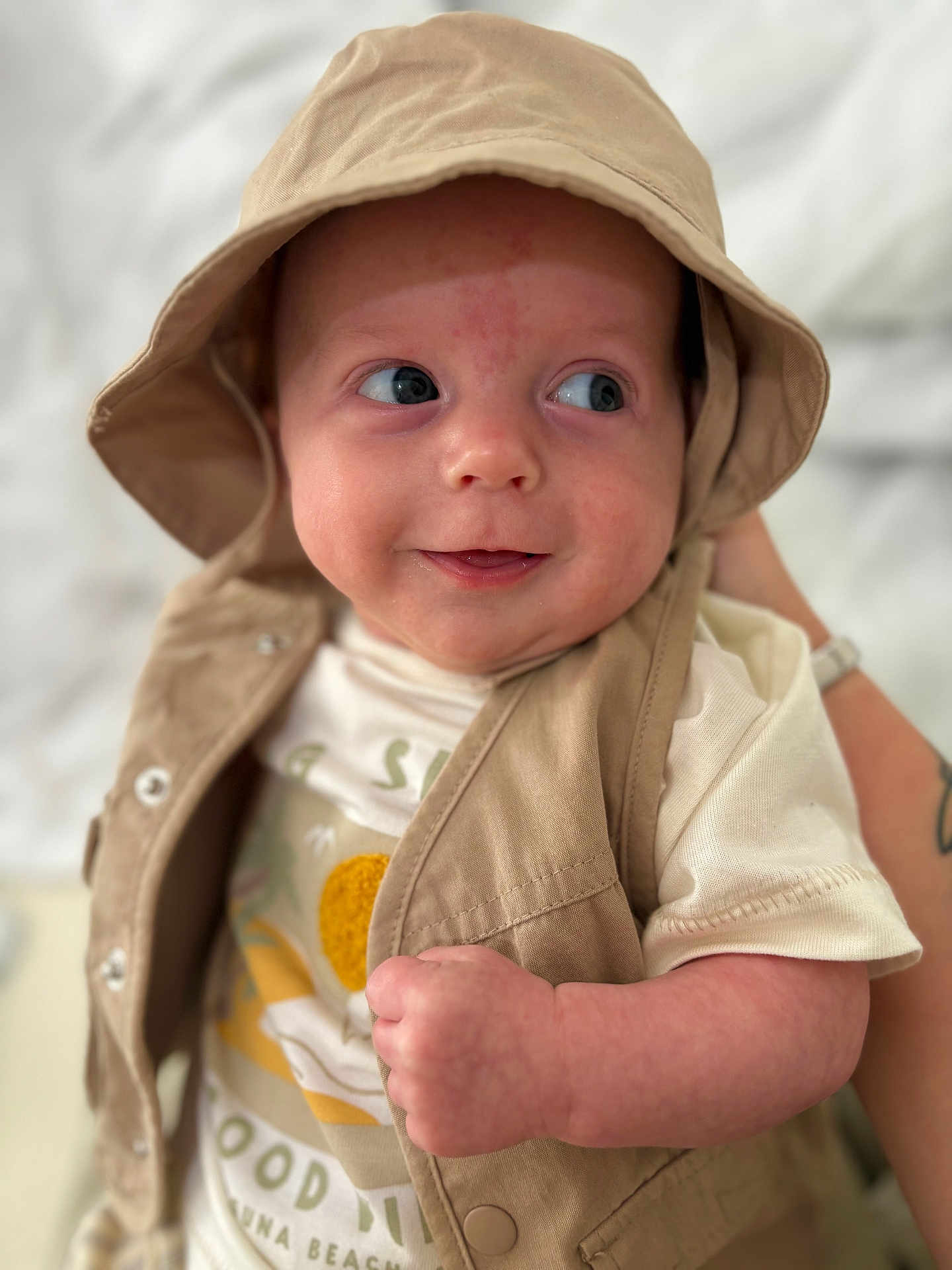 Otto is registered to the contest to win money with this photo: baby, infant, smiling, hat, beige, vest, clothing, face, skin, hand, cute, portrait, person, white_shirt, closeup, expression, child, soft_focus, indoor, happy