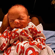 Terrell is registered to the contest to win money with this photo: newborn, baby, infant, sleeping, face, portrait, swaddled, blanket, white_clothing, orange_pattern, adult_hand, indoor, close_up, cozy, resting, head, eyes_closed, nose, mouth, family