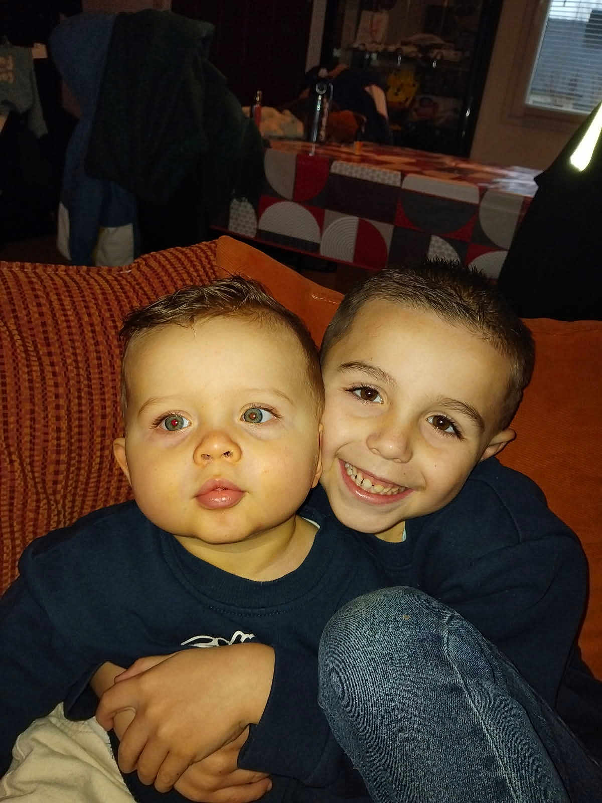 Marlone participe au concours pour gagner de l'argent avec cette photo : child, baby, toddler, brothers, siblings, smiling, couch, indoor, portrait, close_up, hug, family, denim, sweater, red_eye, living_room, pillow, couch_cushion, human_face, cozy