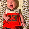 baby, infant, smiling, laughing, child, jersey, number_23, plaid_shorts, blanket, knitted, happy, cute, portrait, lying_down, indoor, skin, face, hand, clothing, colorful