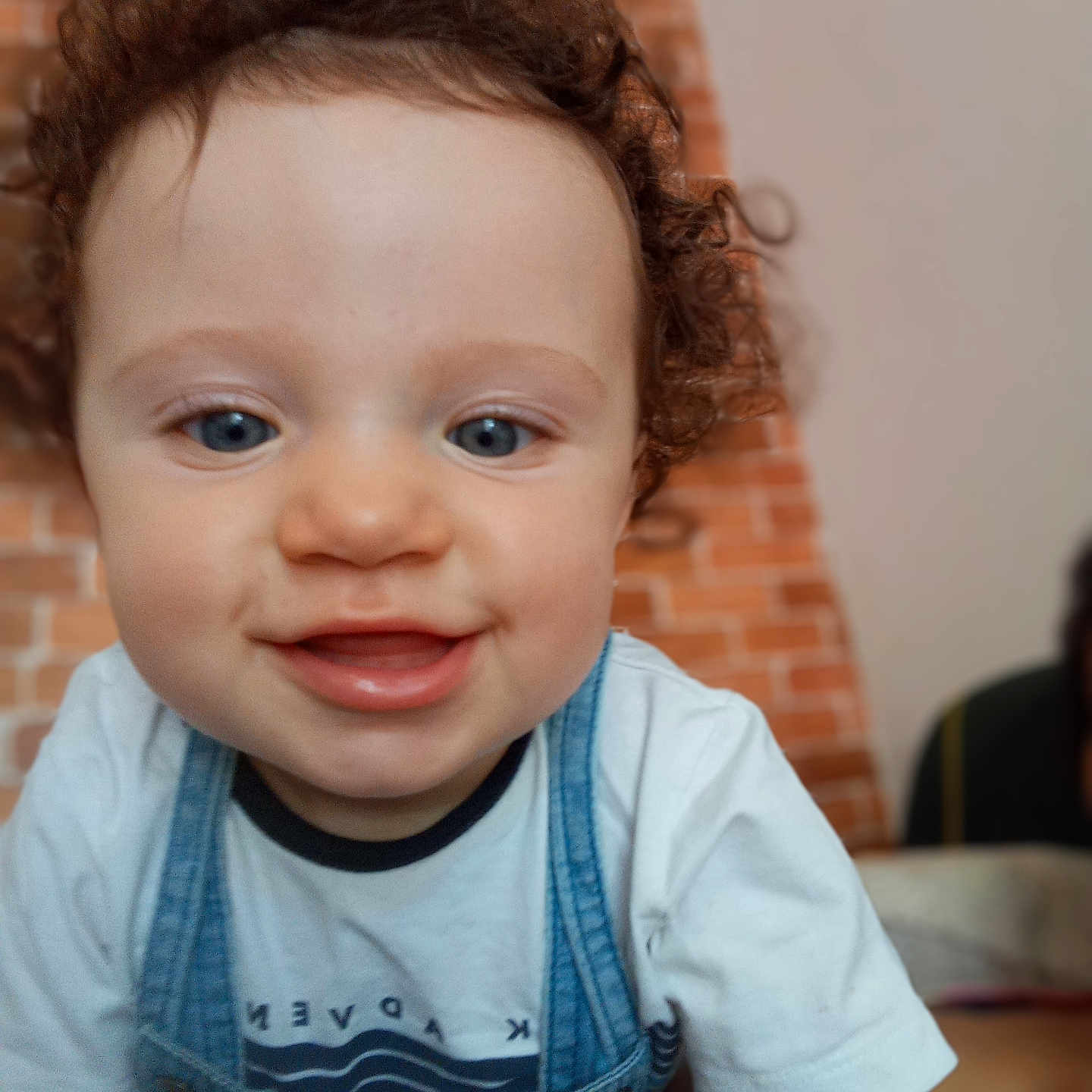 Gabriel a rejoint le concours — aidez-le/la à gagner de superbes lots ! baby, background_blur, blue_eyes, brick_wall, child, close_up, curiosity, curly_hair, cute, denim_overalls, face, happy, indoor, person, portrait, smiling, soft_focus, toddler, white_tshirt, young_child