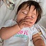 baby, child, infant, toddler, onesie, hand, face, eyes_closed, blanket, bed, sleepy, cute, messy_hair, lying_down, soft_texture, cozy, indoor, person, young_child, sleepwear