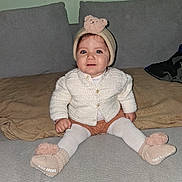 Sarah a rejoint le concours — aidez-le/la à gagner de superbes lots ! baby, child, sitting, knitwear, hat, teddy_bear, socks, couch, blanket, cozy, cute, indoor, portrait, smile, happy, person, face, blue_eyes, warm, infant