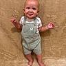 baby, toddler, child, standing, overalls, striped_clothing, cactus_patch, white_shirt, barefoot, carpet, beige_background, smiling, portrait, indoors, cute, happy, face, head, skin, person