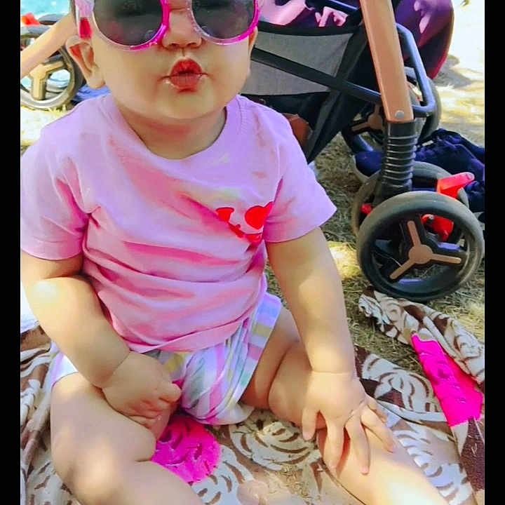 Taqdeer is registered to the contest to win money with this photo: accessory, baby, blanket, child, cute, footwear, funny_face, grass, outdoor, pink_shirt, playtime, pucker, sandals, shorts, sitting, stroller, summer, sunglasses, sunlight, toddler