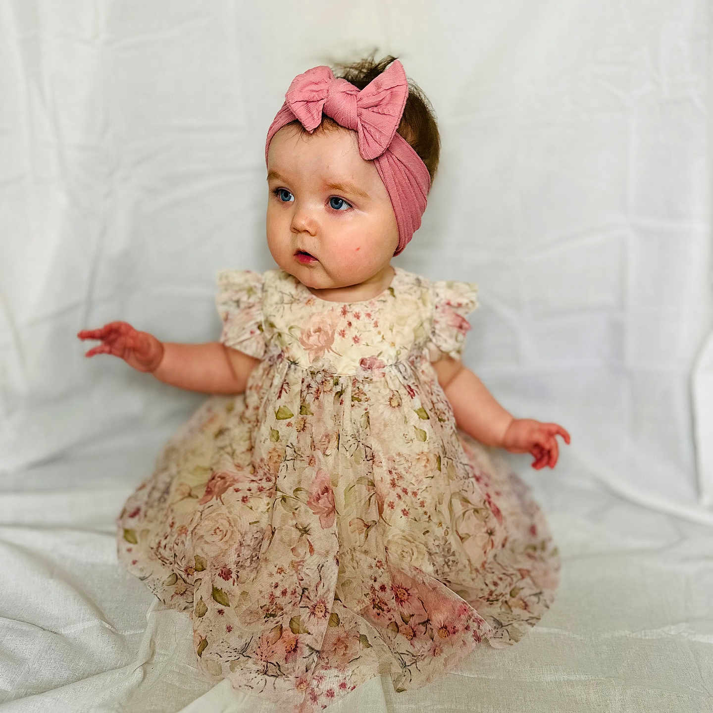 Nora-Irene is registered to the contest to win money with this photo: apparel, baby, blue_eyes, bow, child, curious, cute, dress, fabric, floral, girl, headband, indoors, infant, pattern, pink, portrait, sitting, soft_background, young