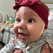 Hadyn joined the competition — help win amazing prizes! baby, child, headband, bow, blue_eyes, floral_clothing, onesie, hand, indoor, living_room, couch, blurred_background, cute, smiling, happy, portrait, person, infant, closeup, skin
