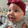 baby, child, headband, bow, blue_eyes, floral_clothing, onesie, hand, indoor, living_room, couch, blurred_background, cute, smiling, happy, portrait, person, infant, closeup, skin