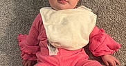 Lyra is registered to the contest to win money with this photo: baby, child, pink_clothing, bib, carpet, floor, indoor, person, cute, infant, looking_at_camera, casual, texture, home, toddler, sitting, face, hands, feet, cables