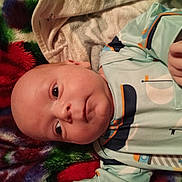 Alijah is registered to the contest to win money with this photo: baby, infant, newborn, blanket, onesie, face, eyes, hand, towel, fabric, soft_texture, plush, lying_down, portrait, close_up, indoors, gaze, sleepwear, colorful, cute