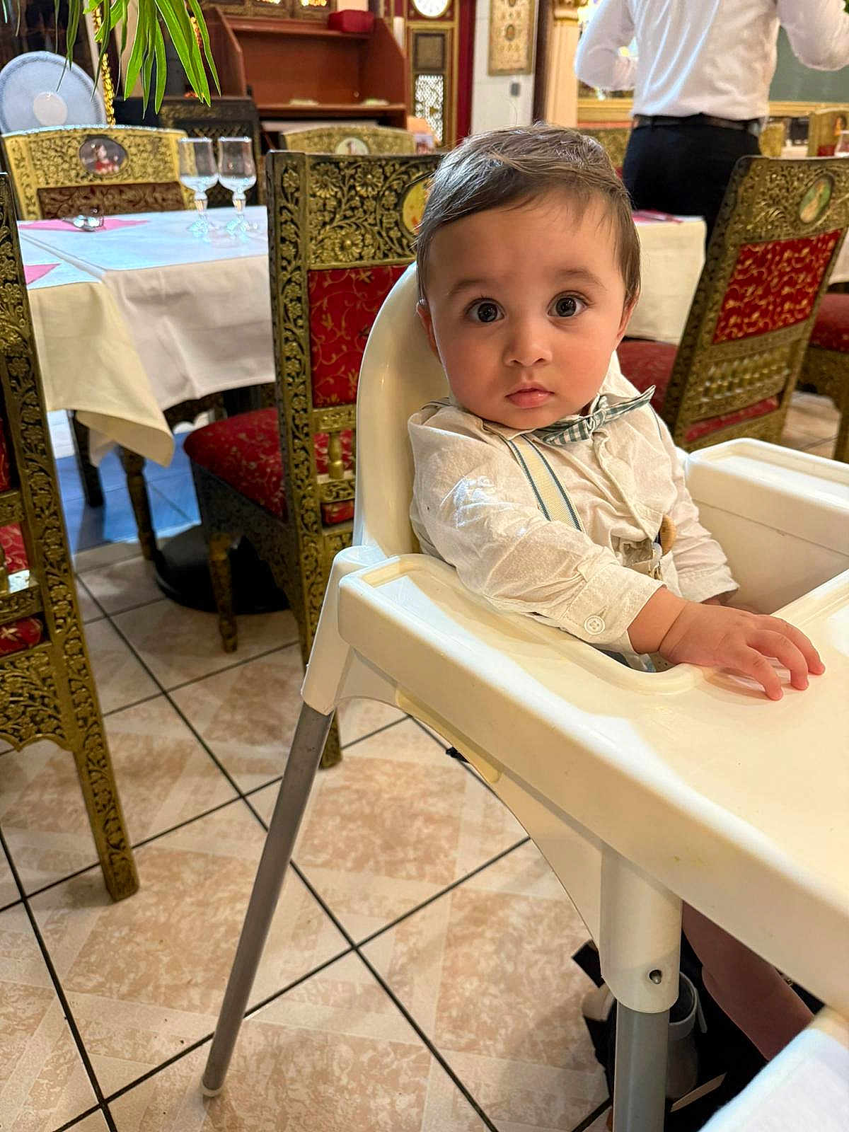 Viaansh participe au concours pour gagner de l'argent avec cette photo : baby, child, high_chair, restaurant, table, chair, floor, person, clothing, bow_tie, face, eyes, hand, tile_floor, waiter, interior, dining, decor, furniture, sitting