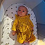 baby, infant, yellow_clothing, headband, playpen, mattress, stars_pattern, lying_down, indoors, cute, child, one_person, looking_at_camera, soft_lighting, small_hands, expression, casual, cozy, comfortable, baby_girl
