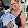 woman, baby, glasses, blanket, headband, pacifier, outdoor, house, porch, smile, person, child, holding, jewelry, tank_top, curly_hair, earrings, nail_polish, denim, footwear