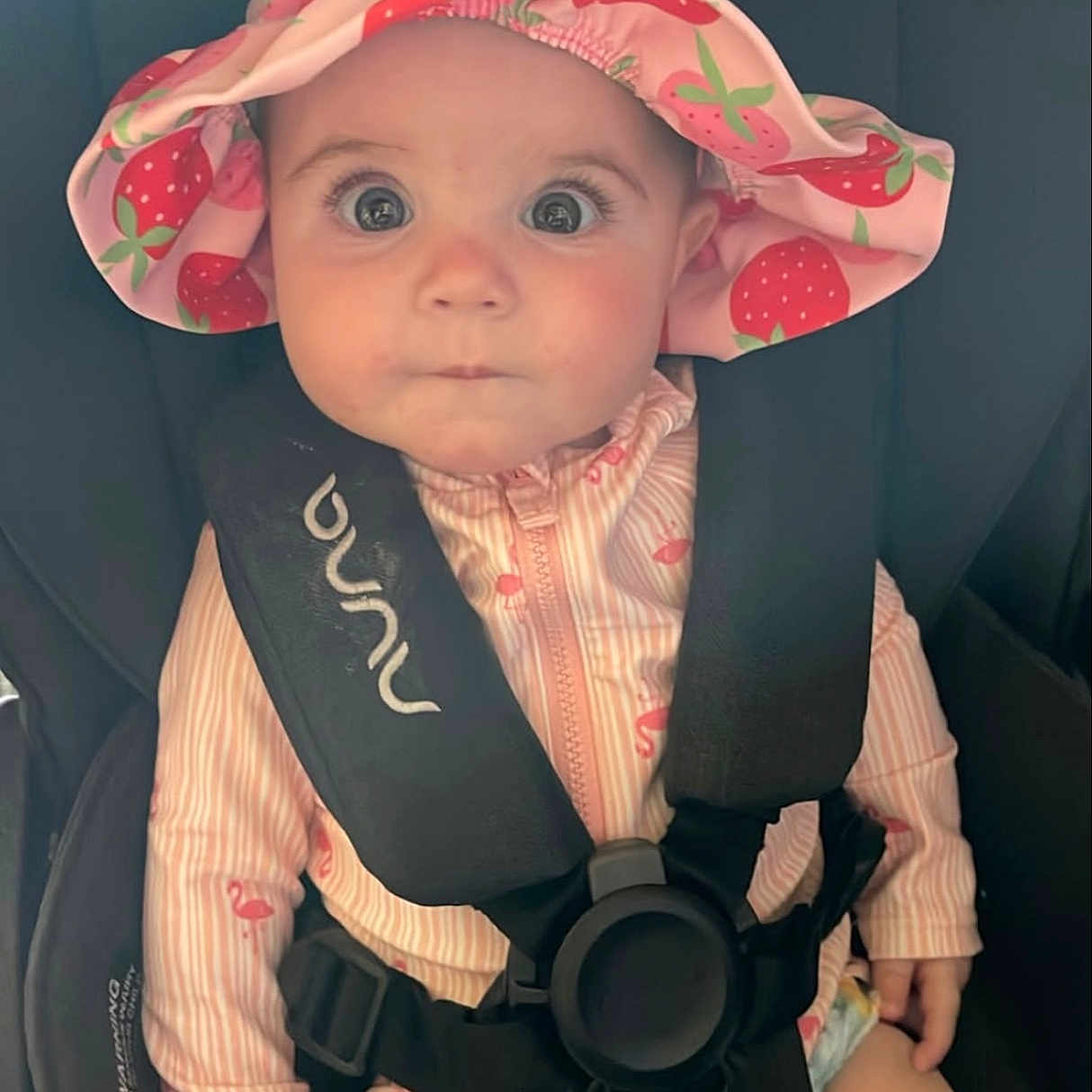 Wrenley joined the competition — help win amazing prizes! baby, car_seat, child, close_up, curious_expression, cute, face, hands, hat, indoor, infant, legs, pink_clothing, portrait, safety_harness, seat_belt, sitting, strawberry_pattern, stripes, wide_eyes