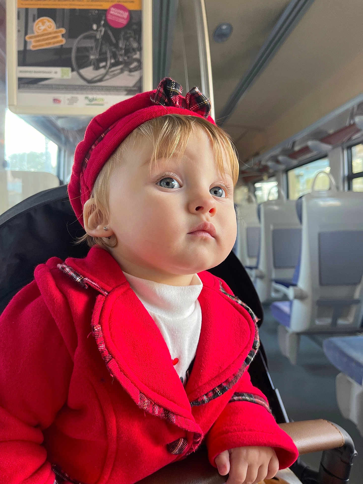 Anastasia a rejoint le concours — aidez-le/la à gagner de superbes lots ! toddler, child, red_coat, hat, blue_eyes, train_interior, window, natural_light, portrait, seated, hand, clothing, face, person, travel, public_transport, cute, young_child, indoor, expression