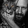 Tom is registered to the contest to win money with this photo: man, beard, bald_head, cat, tabby_cat, animal, pet, portrait, black_and_white, close_up, hand, intense_gaze, face, eyes, fur, whiskers, indoor, bond, human, companion