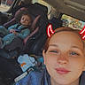 car_interior, child, toddler, car_seat, woman, selfie, hoodie, digital_filter, devil_horns, seatbelt, window, daylight, casual, seat, road, outside_view, child_in_car_seat, portrait, relaxed, smile
