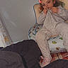 child, pajamas, chair, face, indoors, blanket, toy_story, alien_pattern, cute, cozy, childrens_room, sitting, digital_effect, devil_horns, person, relaxed, soft_lighting, playful, footwear, home