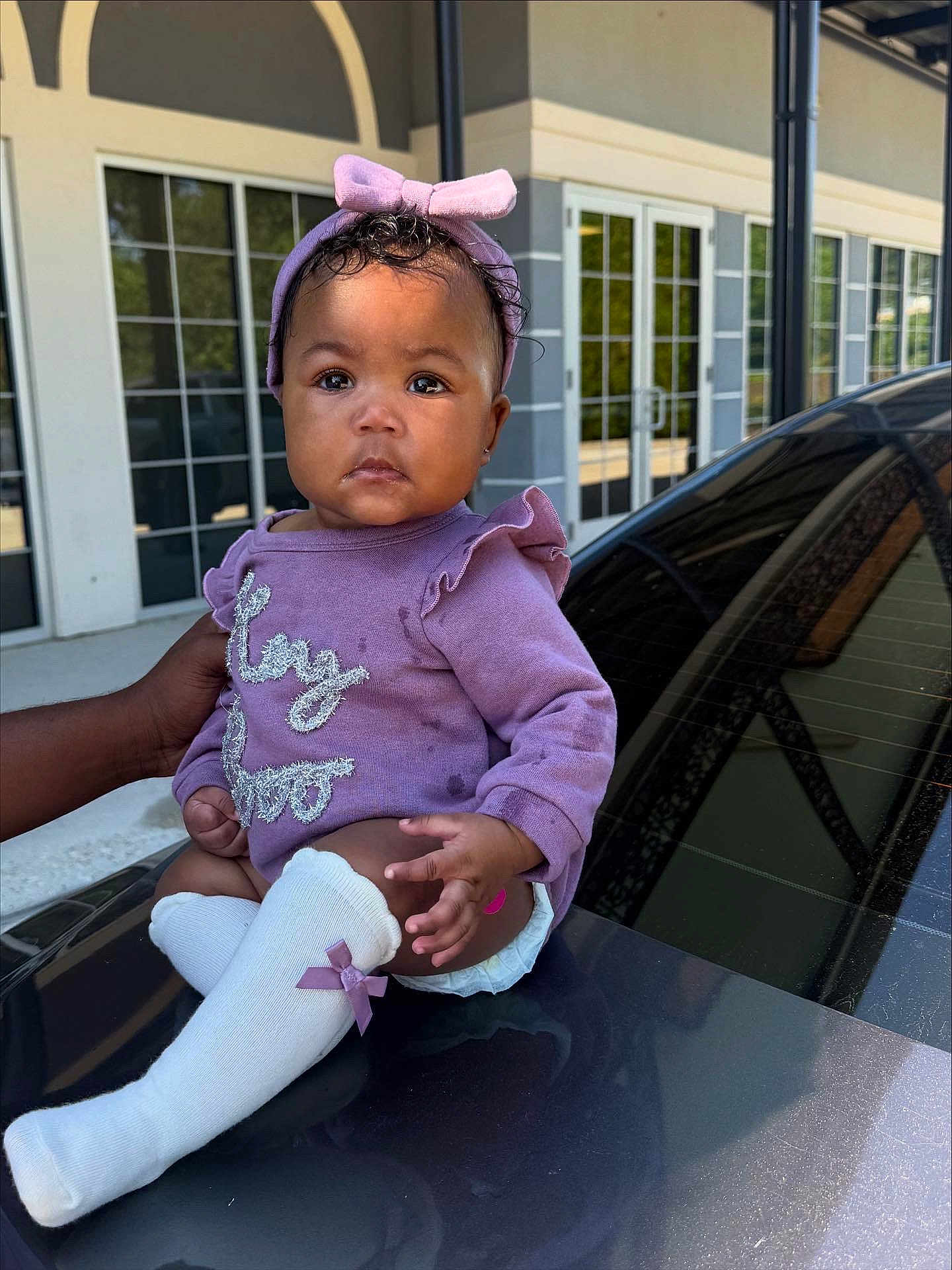 Odyssey joined the competition — help win amazing prizes! baby, child, infant, purple_outfit, headband, car, hand, outdoor, building, glass_doors, curious, sitting, cute, clothing, person, portrait, white_socks, bow, diaper, support