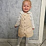 toddler, child, smiling, standing, indoor, dress, white_tights, sneakers, buttoned_dress, long_sleeve_top, floor_tiles, gray_wall, light_hair, cute, happy, portrait, person, fashion, innocence, young