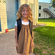 Serenity joined the competition — help win amazing prizes! child, girl, smiling, curly_hair, blonde_hair, leopard_print, dress, backpack, white_shirt, outdoor, sidewalk, grass, building, door, window, sunlight, happy, tattoo, footwear, daylight