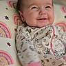 baby, babywear, child, clothing, colorful, cute, face, happy, indoors, infant, lying_down, onesie, pattern, person, pillow, portrait, rainbow, smiling, soft, unicorn