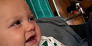 Darien is registered to the contest to win money with this photo: baby, child, face, closeup, christmas, holiday, onesie, clothing, indoor, living_room, furniture, lamp, wood, curtains, expression, person, cute, infant, smiling, cozy