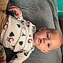 baby, infant, pajamas, christmas_theme, santa_claus, christmas_tree, blanket, toy, indoor, child, face, cute, lying_down, soft_texture, holiday, sleepwear, person, young_child, skin, head