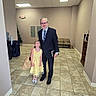 Hope is registered to the contest to win money with this photo: child, girl, adult, man, portrait, smiling, yellow_dress, suit, tie, formalwear, indoor, hallway, tiled_floor, exit_sign, chairs, bookshelf, water_cooler, standing, family, happy