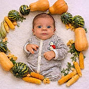 Skander a rejoint le concours — aidez-le/la à gagner de superbes lots ! baby, infant, striped_onesie, face, wide_eyes, pumpkin, gourd, corn, yellow_flower, autumn, circle_arrangement, lying_down, cute, surprised_expression, baby_clothing, soft_surface, harvest, nature, seasonal, decorative
