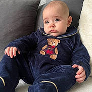 Luca George joined the competition — help win amazing prizes! baby, infant, child, onesie, teddy_bear, blue_clothing, couch, pillow, soft_texture, indoor, portrait, cute, plush, relaxed, sitting, expression, face, hand, foot, person