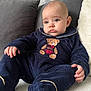 baby, infant, child, onesie, teddy_bear, blue_clothing, couch, pillow, soft_texture, indoor, portrait, cute, plush, relaxed, sitting, expression, face, hand, foot, person