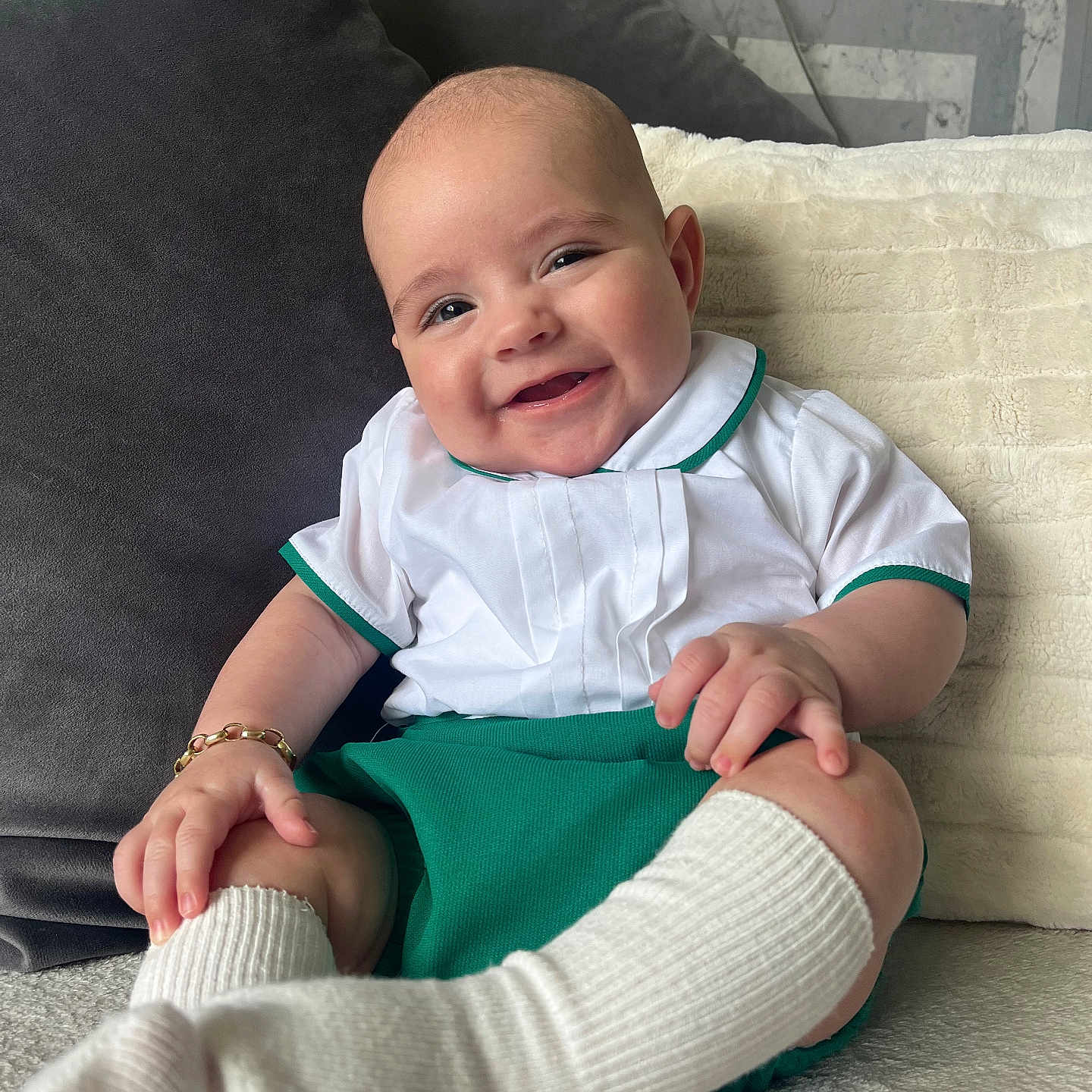 Luca George is registered to the contest to win money with this photo: baby, bracelet, child, clothing, couch, cozy, cute, green_shorts, happy, indoor, infant, person, pillow, portrait, sitting, smile, soft_texture, white_shirt, white_socks, young_child