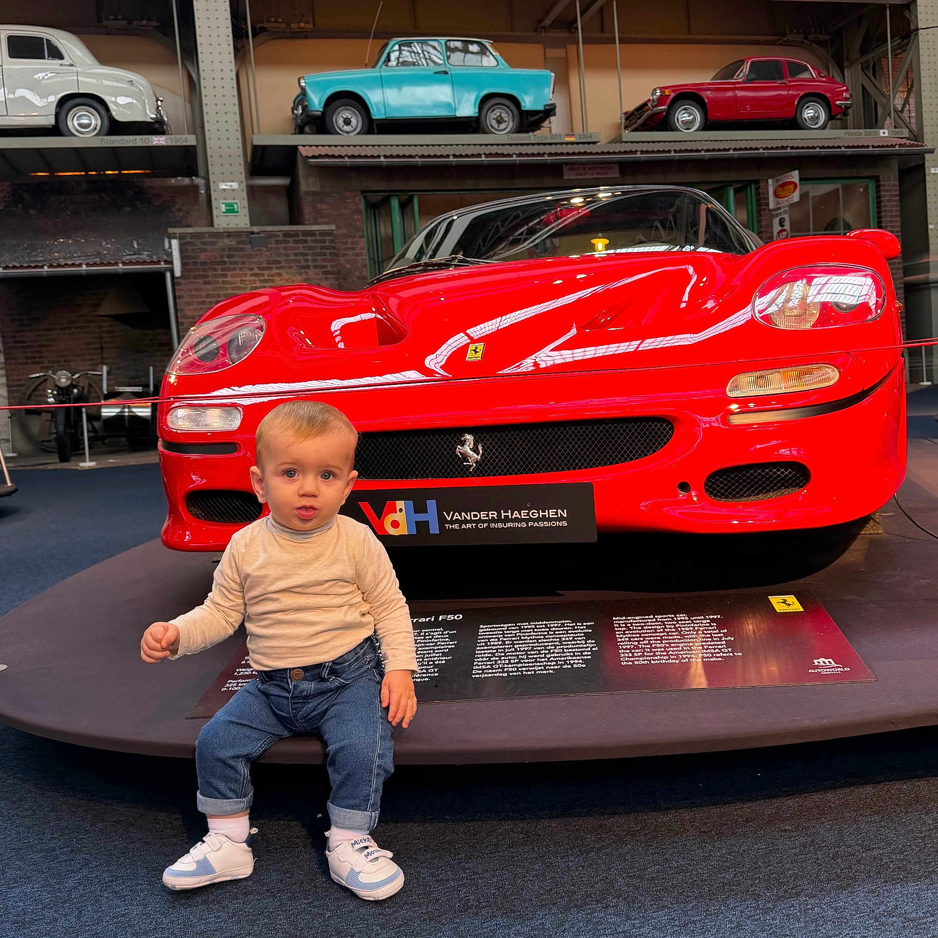 Theo participe au concours pour gagner de l'argent avec cette photo : automobile, baby, car, child, clothing, curious, display, exhibit, ferrari, floor, head, indoor, jeans, museum, person, red_car, sneakers, toddler, vehicle, vintage_car
