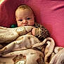 animal_print, baby, blanket, child, clothing, comfort, cozy, cute, expression, face, hand, indoors, infant, lying_down, pink_background, portrait, soft, texture, warm, young
