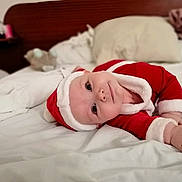 Phœbe a rejoint le concours — aidez-le/la à gagner de superbes lots ! baby, child, santa_outfit, bed, blanket, pillow, indoors, cute, lying_down, face, infant, holiday, christmas, soft_texture, smiling, red_clothing, white_trim, head_tilt, cozy, sleepwear