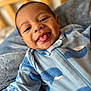 baby, infant, blue_onesie, whale_print, tongue_out, smiling, face, head, blanket, bed, crib, wooden_furniture, soft_texture, cute, closeup, indoors, child, playful, happy, person