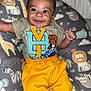 baby, smiling, child, infant, yellow_pants, graphic_tee, cushion, animal_print, giraffe, lion, zebra, elephant, happy, cute, portrait, indoors, clothing, person, bright_colors, baby_boy