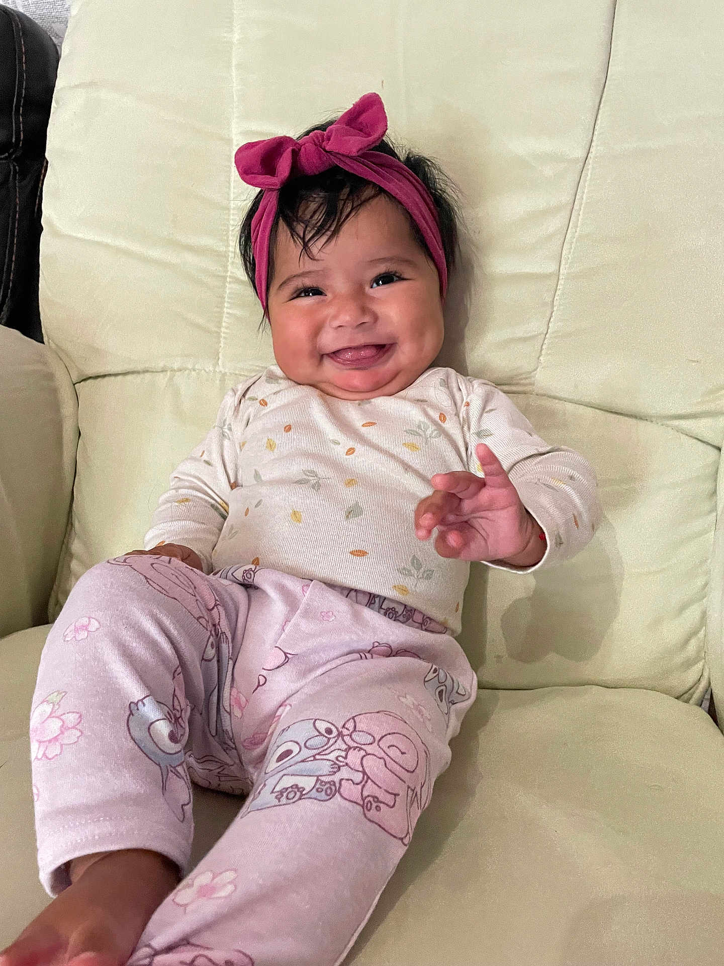 Aurora is registered to the contest to win money with this photo: baby, smiling, headband, pink, pajamas, patterned_clothing, cushion, chair, indoors, comfort, happy, person, infant, cute, child, sitting, hand_gesture, face, hair, relaxed