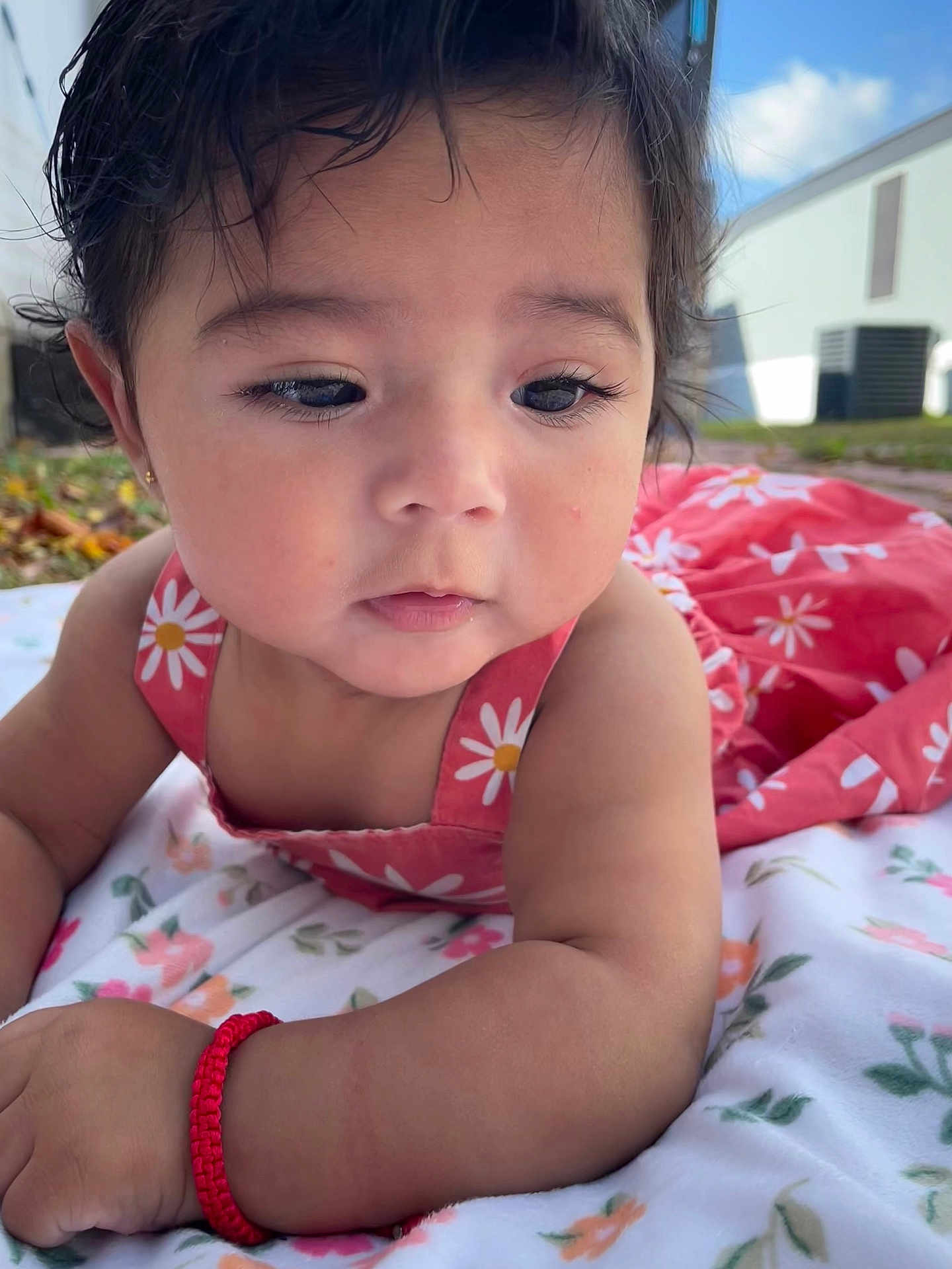 Aurora is registered to the contest to win money with this photo: baby, child, infant, outdoor, blanket, dress, flower_pattern, bracelet, skin, face, cute, young_child, nature, daylight, expression, lying_down, portrait, closeup, person, eyes