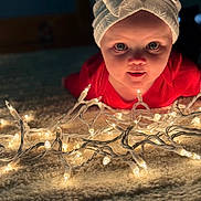 Piper joined the competition — help win amazing prizes! baby, child, headband, bow, lights, string_lights, carpet, indoor, curious, face, portrait, glowing, soft, red_clothing, closeup, infant, toddler, decorative_lights, warm_lighting, holiday
