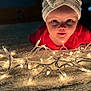 baby, child, headband, bow, lights, string_lights, carpet, indoor, curious, face, portrait, glowing, soft, red_clothing, closeup, infant, toddler, decorative_lights, warm_lighting, holiday