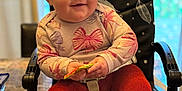 Piper is registered to the contest to win money with this photo: baby, child, high_chair, red_tights, floral_shirt, smiling, indoor, table, snack, curly_hair, happy, seated, furniture, cute, face, person, home, cozy, bright_eyes, infant