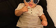 Joziah joined the competition — help win amazing prizes! baby, child, sunglasses, striped_clothing, cushion, black_background, indoor, smiling, cute, fashion, infant, relaxed, person, portrait, shorts, shirt, comfort, seated, hand, playful