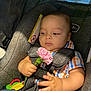 Joziah joined the competition — help win amazing prizes! baby, child, car_seat, flower, pink_carnation, holding, toy, pacifier, plaid_shirt, blue_jeans, safety_harness, infant, cute, indoor, seat_belt, close_up, person, face, hand, curious