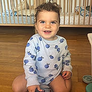 Andrea participe au concours pour gagner de l'argent avec cette photo : toddler, child, toy_car, police_car, curly_hair, smiling, indoor, wooden_floor, crib, cushions, long_sleeve, blue_pattern, play, happy, person, furniture, home, floor, cute, baby