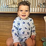 toddler, child, toy_car, police_car, curly_hair, smiling, indoor, wooden_floor, crib, cushions, long_sleeve, blue_pattern, play, happy, person, furniture, home, floor, cute, baby