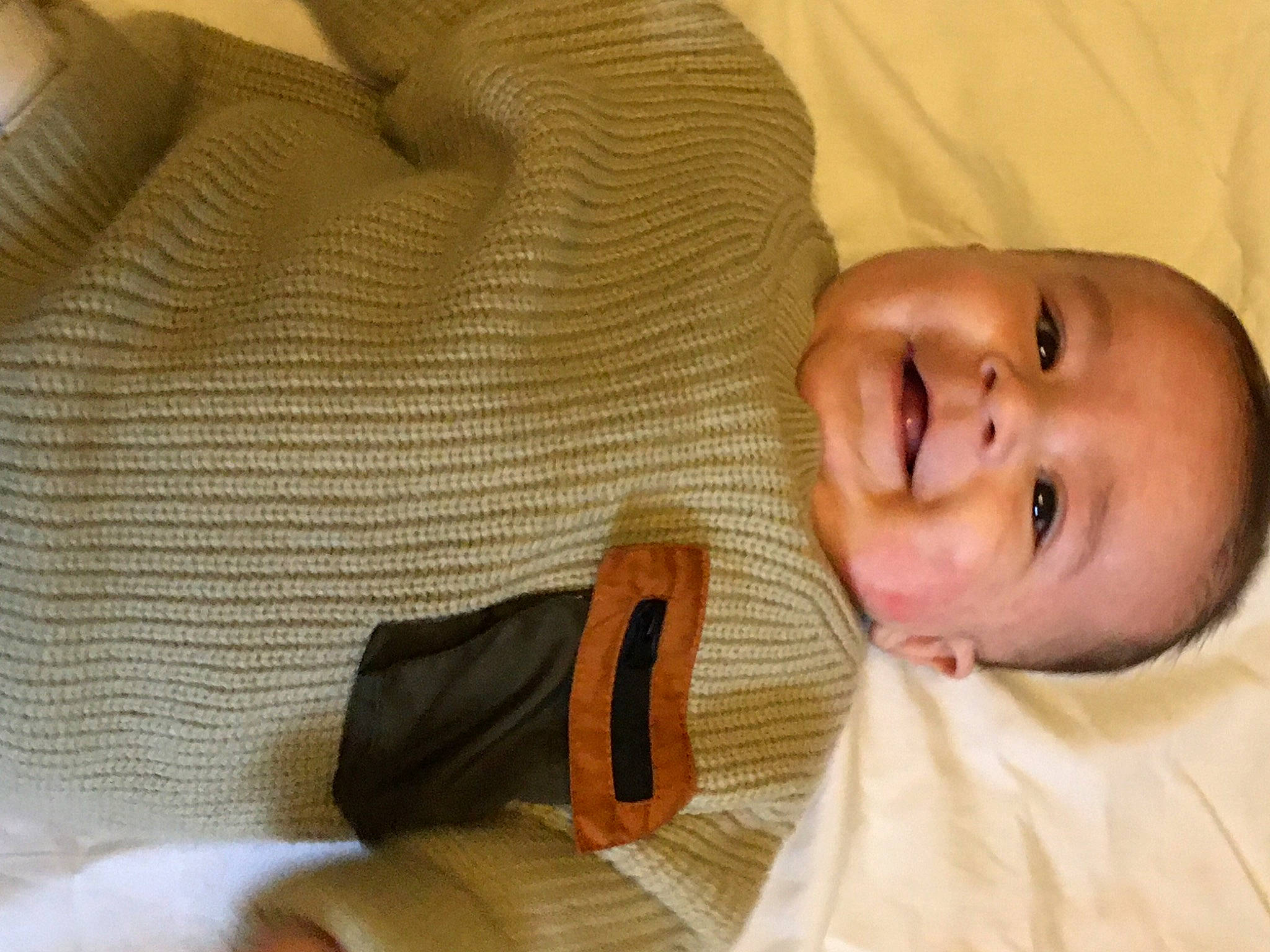 Enoch is registered to the contest to win money with this photo: arm, baby, baby_toddler_clothing, comfort, eyebrow, finger, gesture, hand, human_body, mouth, neck, nose, organ, outerwear, person, skin, sleeve, smile, textile, thumb