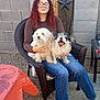 Mico joined the competition — help win amazing prizes! person, woman, glasses, curly_hair, wicker_chair, dog, white_dog, black_and_white_dog, smiling_dog, outdoor, casual_clothing, jeans, brown_shirt, black_socks, gravel_ground, wooden_post, decorative_stars, table, orange_tablecloth, happy